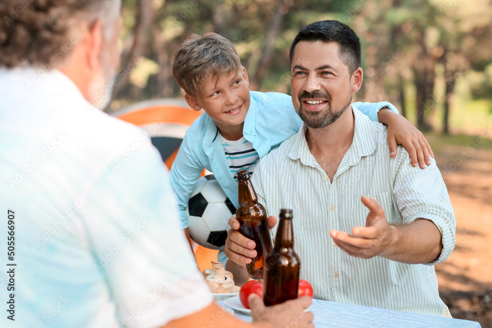 夏日烧烤派对上，一个英俊的男人带着一瓶啤酒和他的小儿子