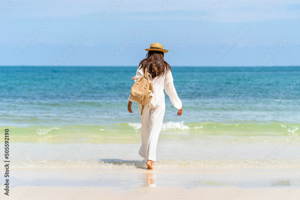 戴草帽带袋子的女人站在海滩上