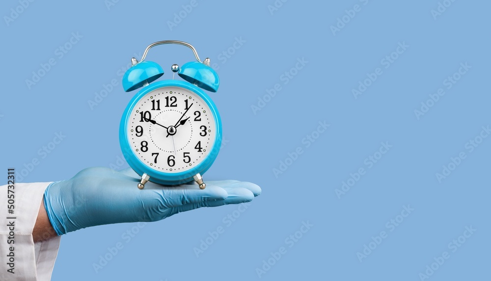 医生们手拿蓝色背景上的闹钟。时间是至关重要的生命概念。