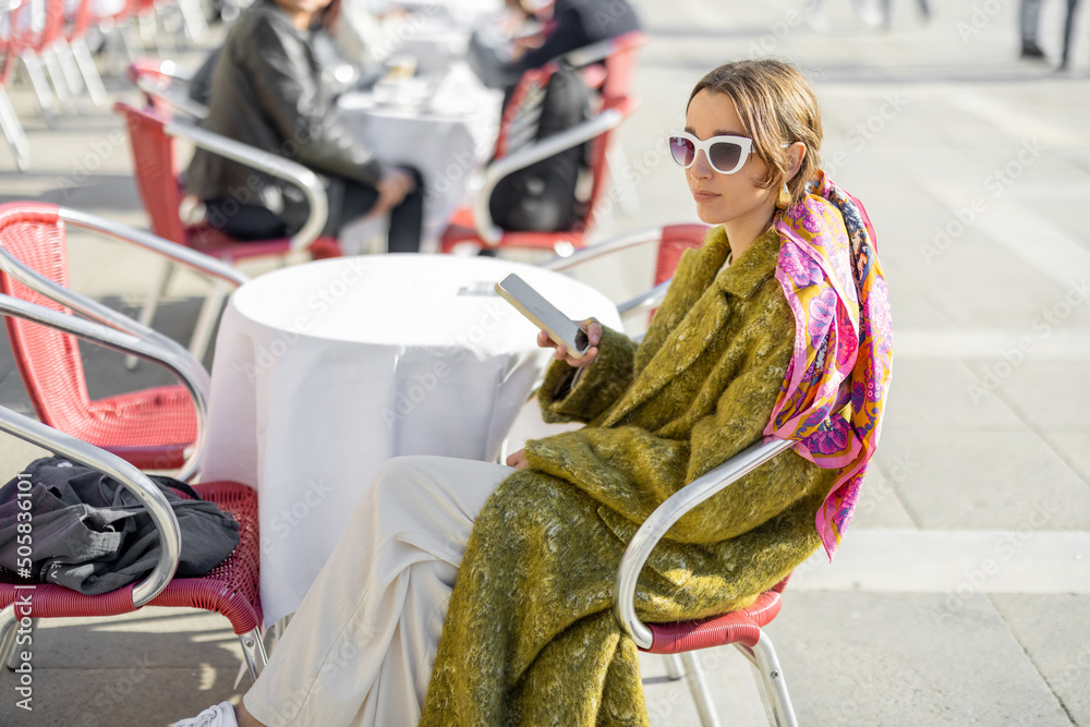 Young woman with phone sitting at outdoor cafe on the famous saint Marks square in Venice. Concept o