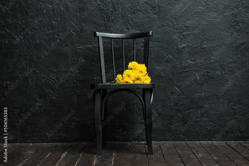 深色墙壁附近开着黄色花朵的黑色椅子