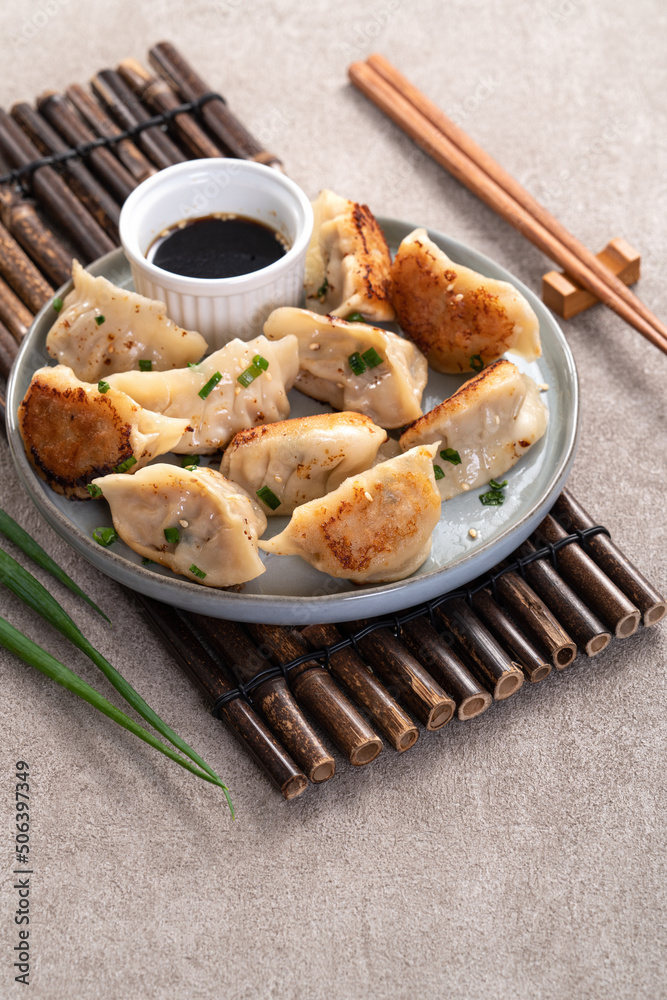 灰色桌子背景上放着酱油的盘子里的煎饺子饺子饺子。