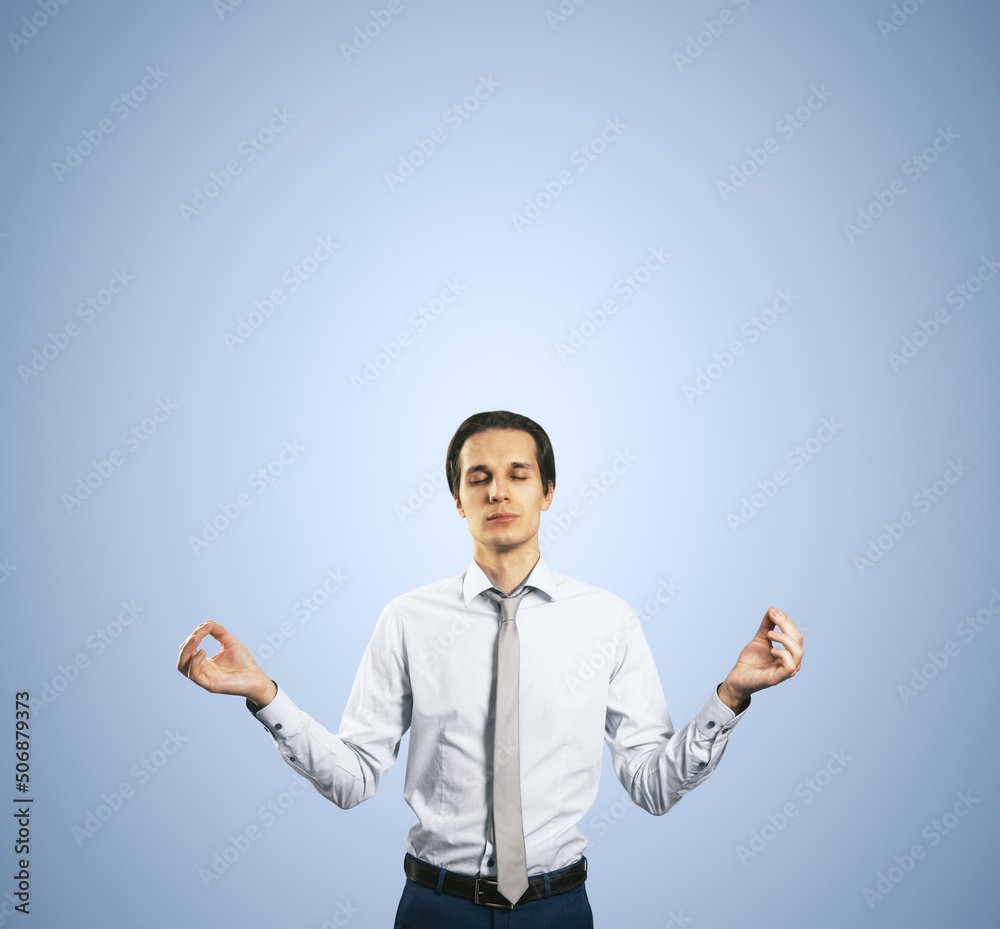 Calm down concept with man in white shirt in a zen pose isolated on light blue wall background with 