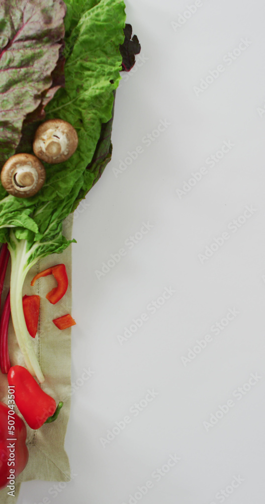 白底上的新鲜辣椒、沙拉叶和蘑菇的垂直图像