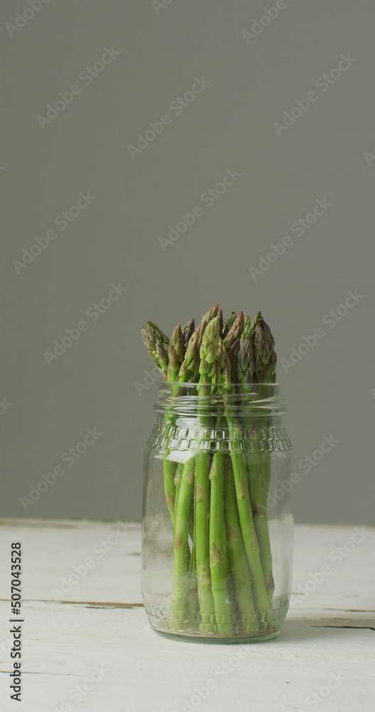 灰色背景下玻璃罐中新鲜芦笋茎的垂直图像