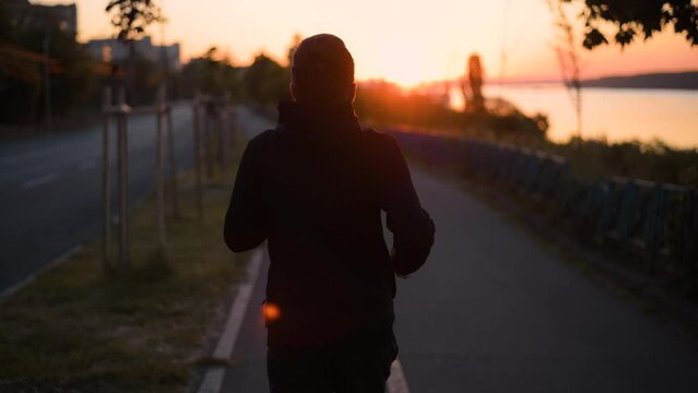 Tracking shot of a man running early in the morning, right after the sunrise, on the sidewalk