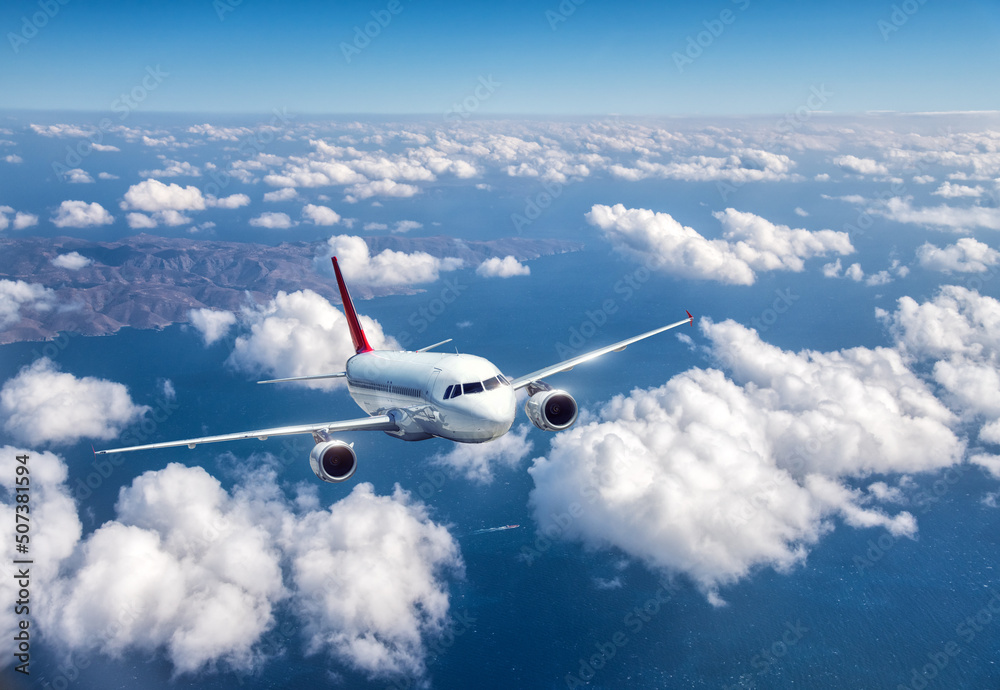 飞机在夏天的云层上方飞行。风景与客机、山脉、蓝色
