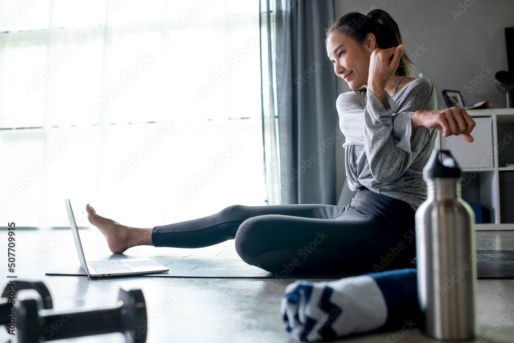 运动型年轻亚洲女性在家锻炼，在互联网上观看健身视频或在线健身