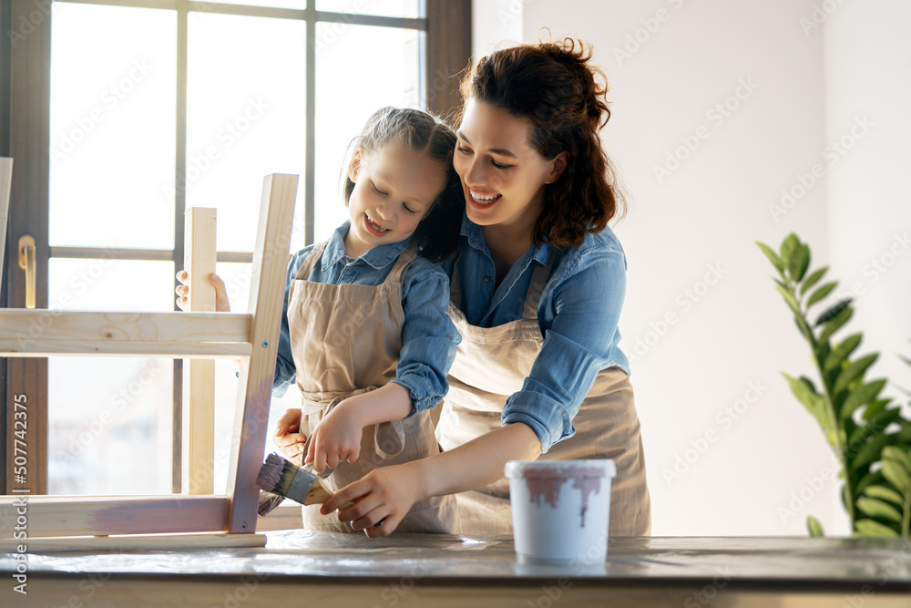 mother and daughter are painting a wooden stool