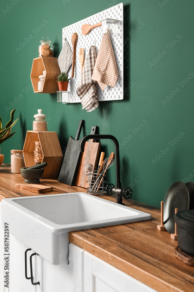 绿色墙壁附近柜台上的带厨房用具和水槽的砧板