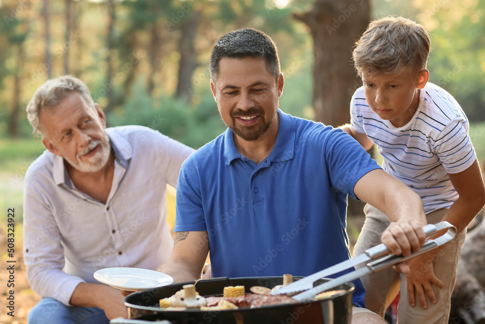 英俊男子在烧烤派对上与父亲和小儿子一起在烤架上烹饪食物