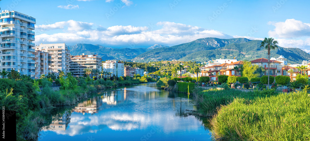 Beautiful river embankment with park area against backdrop of picturesque mountains in city of Alany