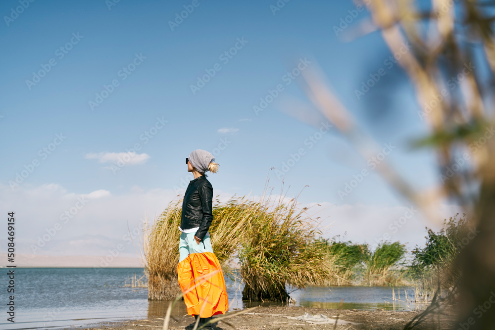 asian woman standing by a lake under blue sky