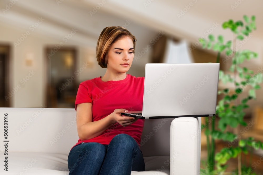 年轻女学生坐在家里的沙发上，在视频通话或在线课堂上使用笔记本电脑