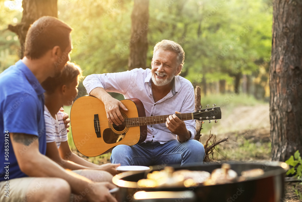 一位老人在夏日烧烤派对上为家人弹吉他