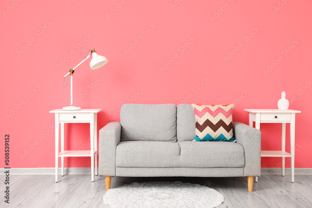 粉色墙壁附近的桌子上有舒适的沙发和现代的灯