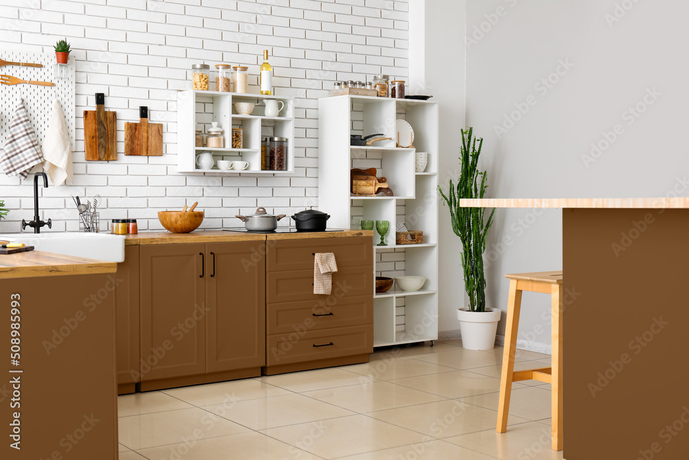 Stylish interior of light kitchen with brown furniture and different utensils