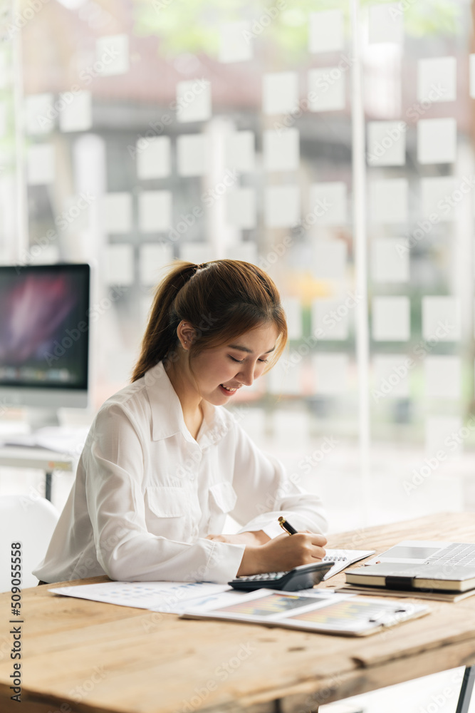 快乐迷人的亚洲商务女性，在办公室拿着笔记本电脑和财务文件工作，成功了