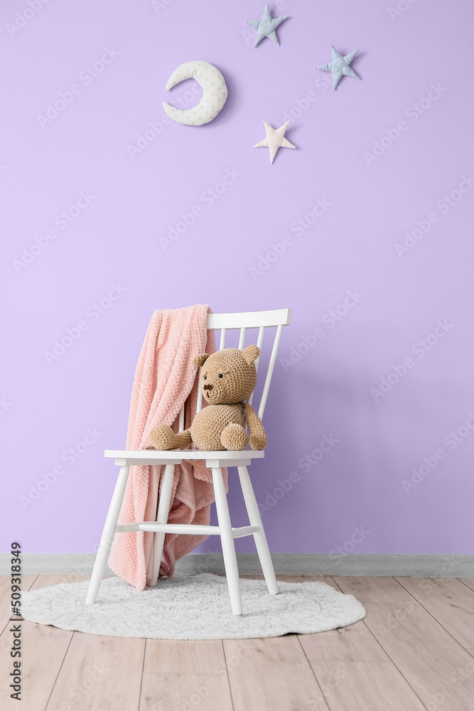 房间内部靠近紫色墙壁的椅子上有玩具熊和软格子