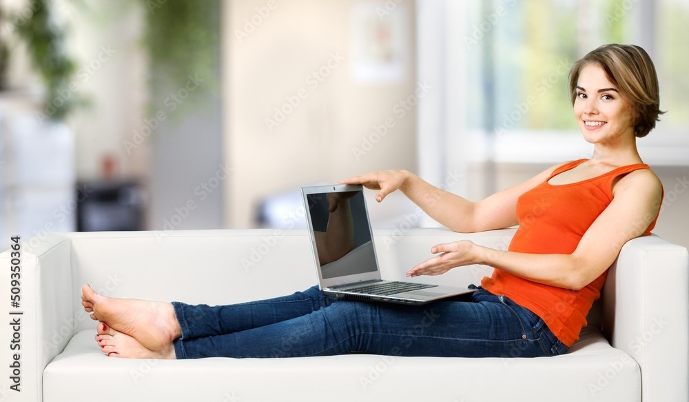 年轻女学生坐在家里的沙发上，在视频通话或在线课堂上使用笔记本电脑