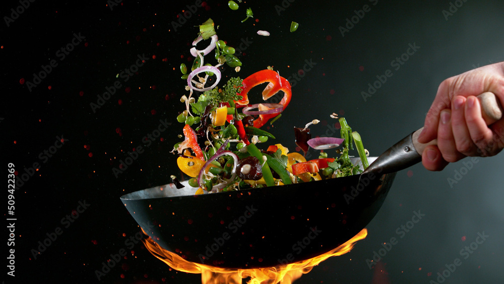 厨师把炒锅里的蔬菜混合物扔进火里的特写镜头。