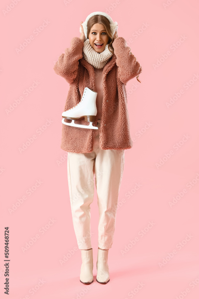 Beautiful happy young woman with ice skates on pink background