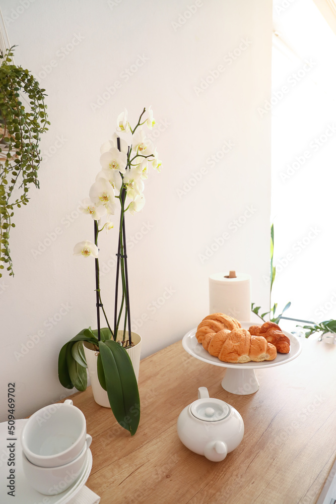 白色墙壁附近厨房柜台上美味的羊角面包、餐具和兰花