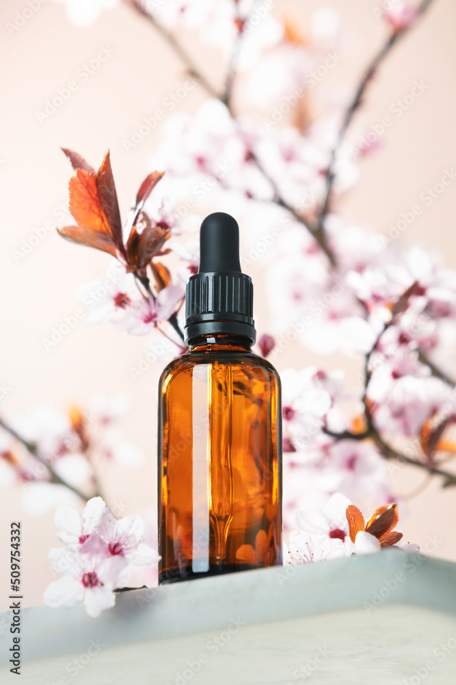 Amber glass dropper bottle and spring cherry blossom flower on marble shelf.  Skincare products , na