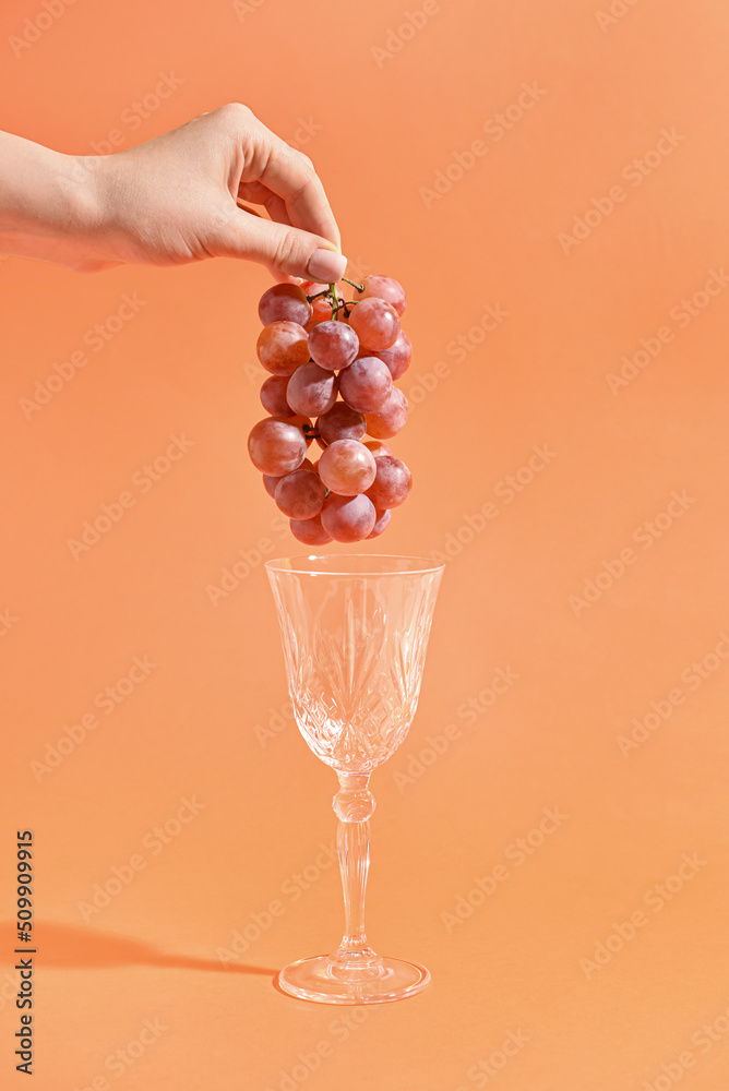 Woman holding fresh grapes and wine glass on color background