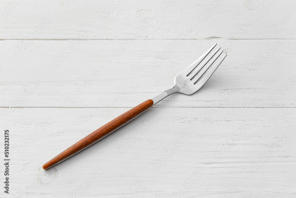 Stylish stainless steel fork on white wooden background