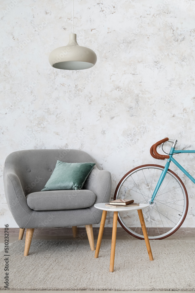 Comfortable armchair, table and bicycle near light wall in living room interior