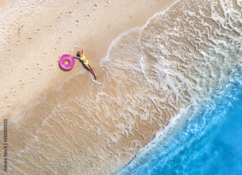 戴着粉色游泳圈躺在海边沙滩上的美丽年轻女子的鸟瞰图