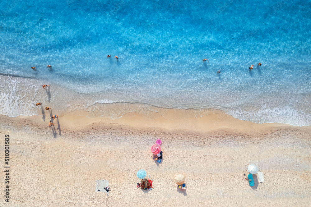 夏天日落时，漂浮的大海、海浪、沙滩和躺着的人的雨伞的鸟瞰图。