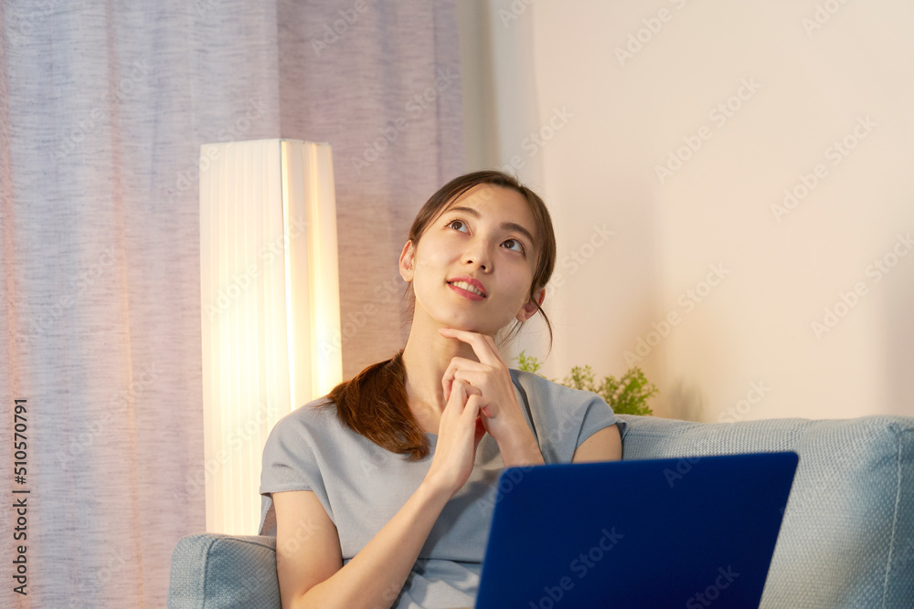 夜のリビングでノートパソコンを使いながら考える女性