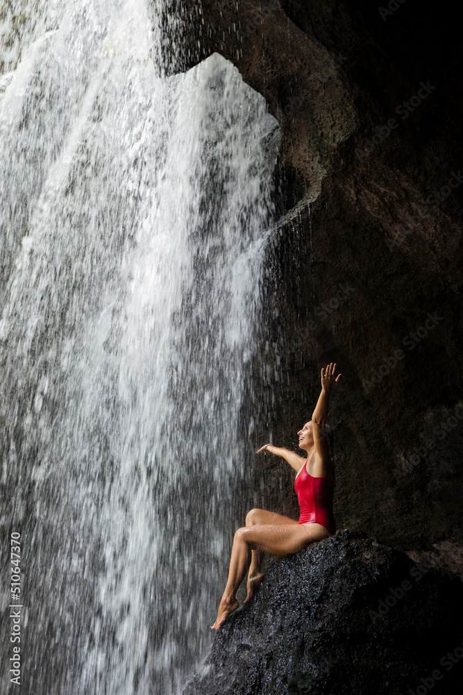 热带丛林中，一名身穿比基尼的女子坐在苏瓦特瀑布瀑布下的岩石上。自然日到