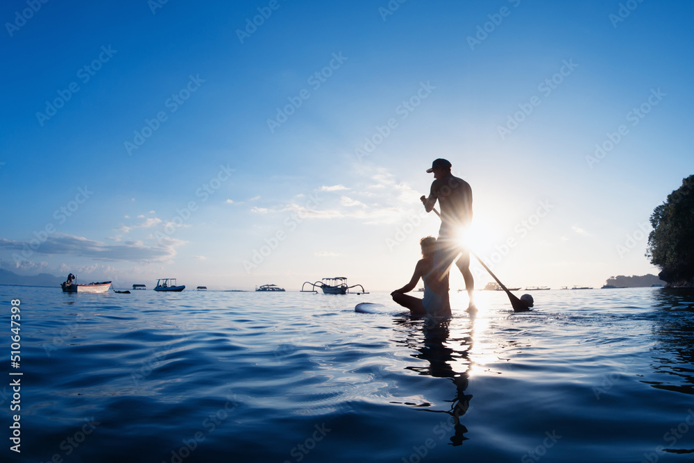 年轻幸福的夫妇在立式桨板上玩得很开心。活跃的桨板手在日落的海边划水。H