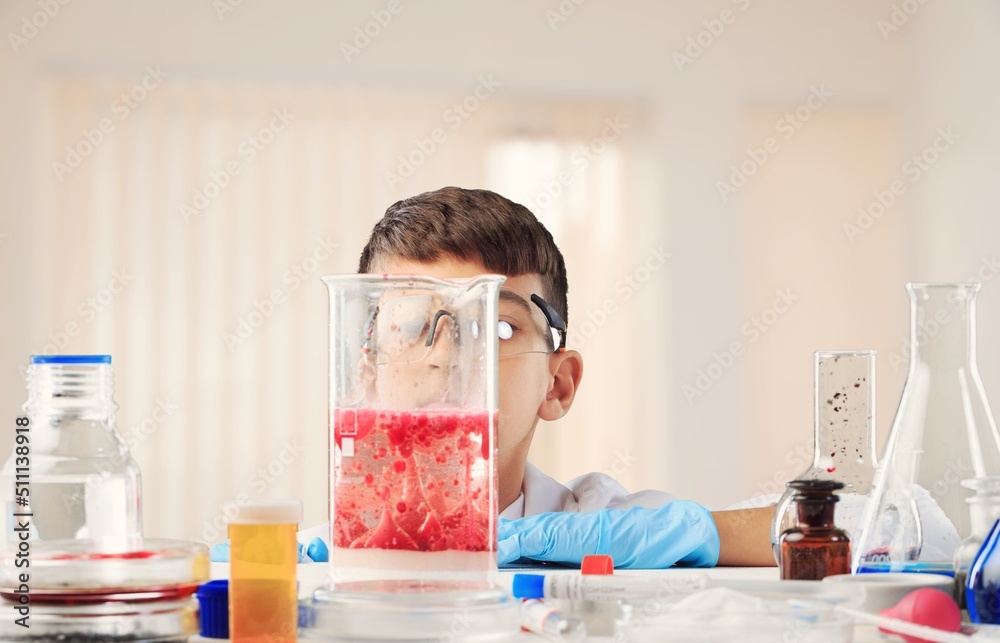 科学化学实验中的聪明男孩戴着防护眼镜，拿着装有liq的瓶子