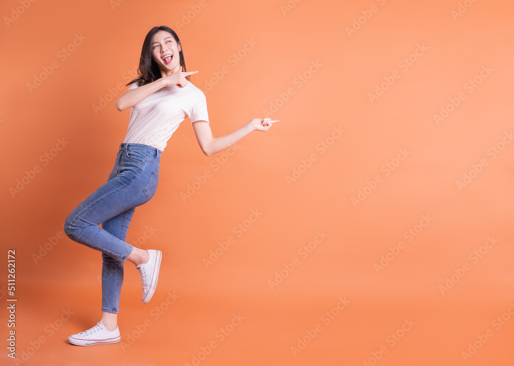 年轻亚洲女性在橙色背景下摆姿势的全长照片