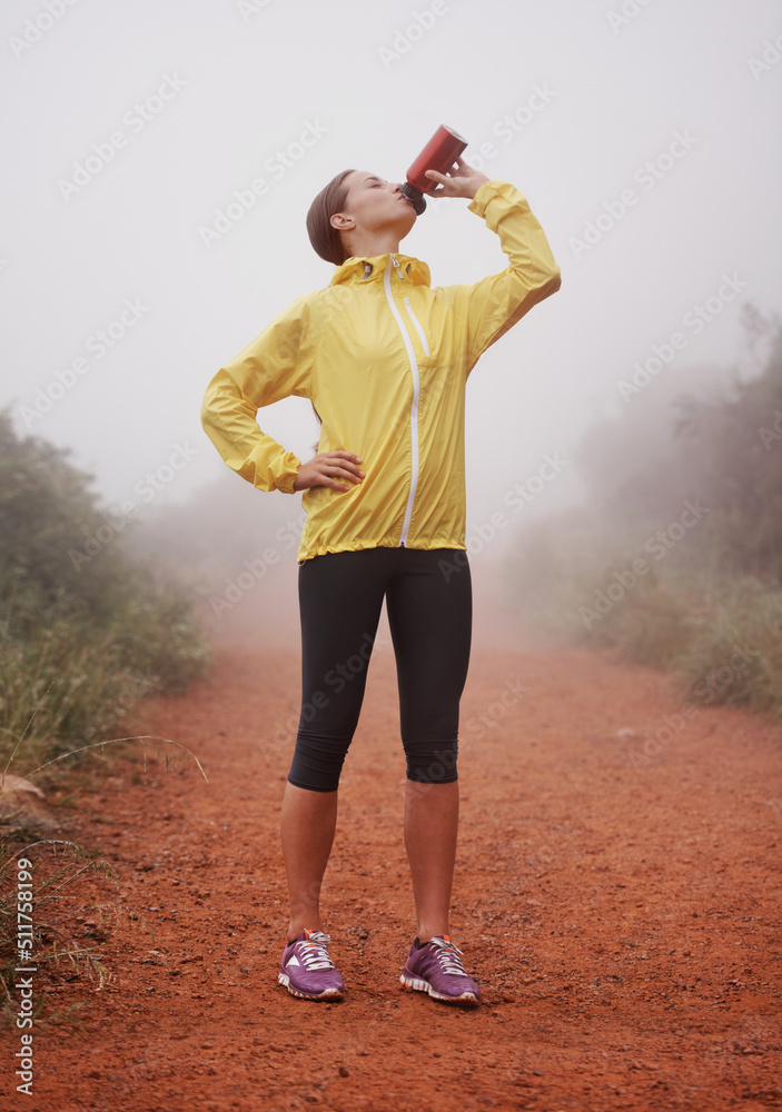 一路上喝了一杯。一名年轻的女跑步者站在前面用水瓶喝水