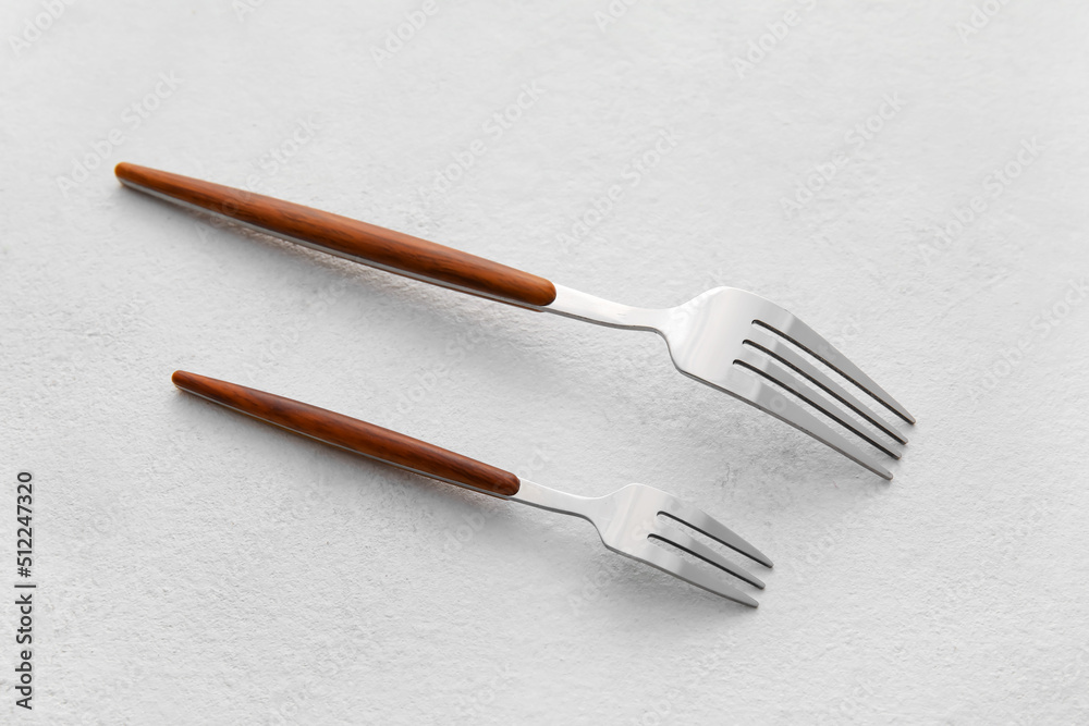Stylish stainless steel forks on light background