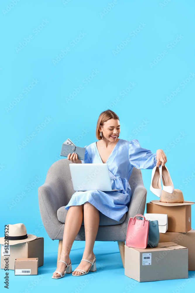 蓝底带笔记本电脑、钱包和新衣服的年轻女子。网上购物