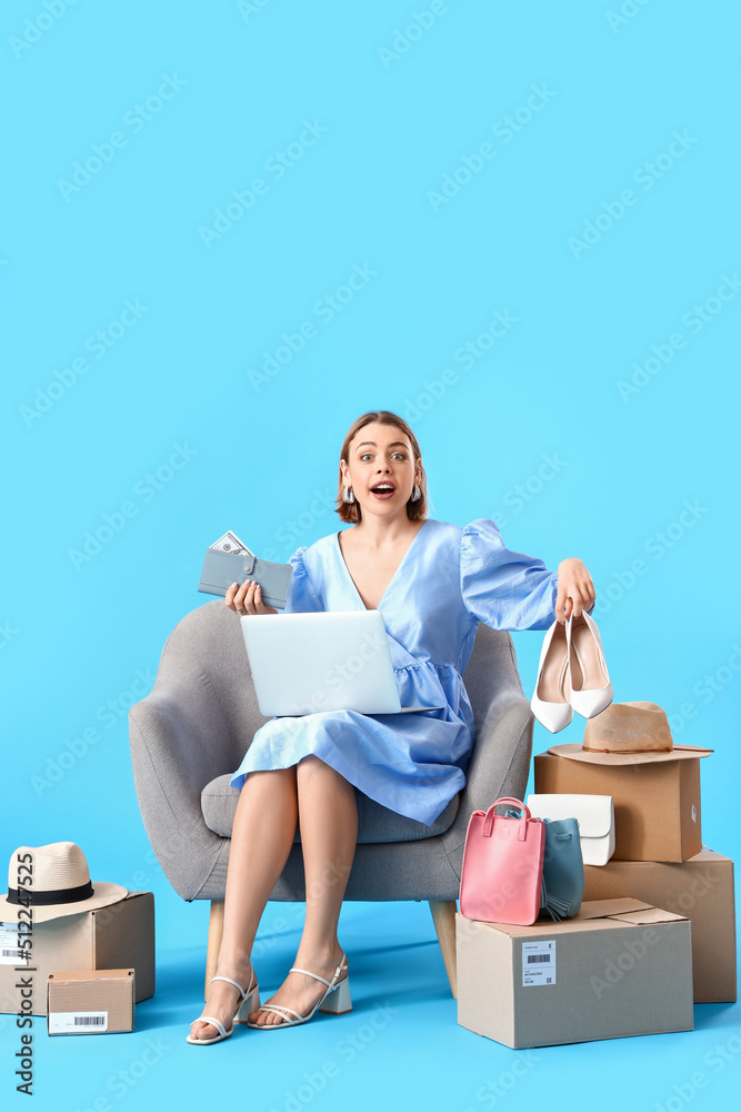Young woman with laptop, wallet and new clothes on blue background. Online shopping