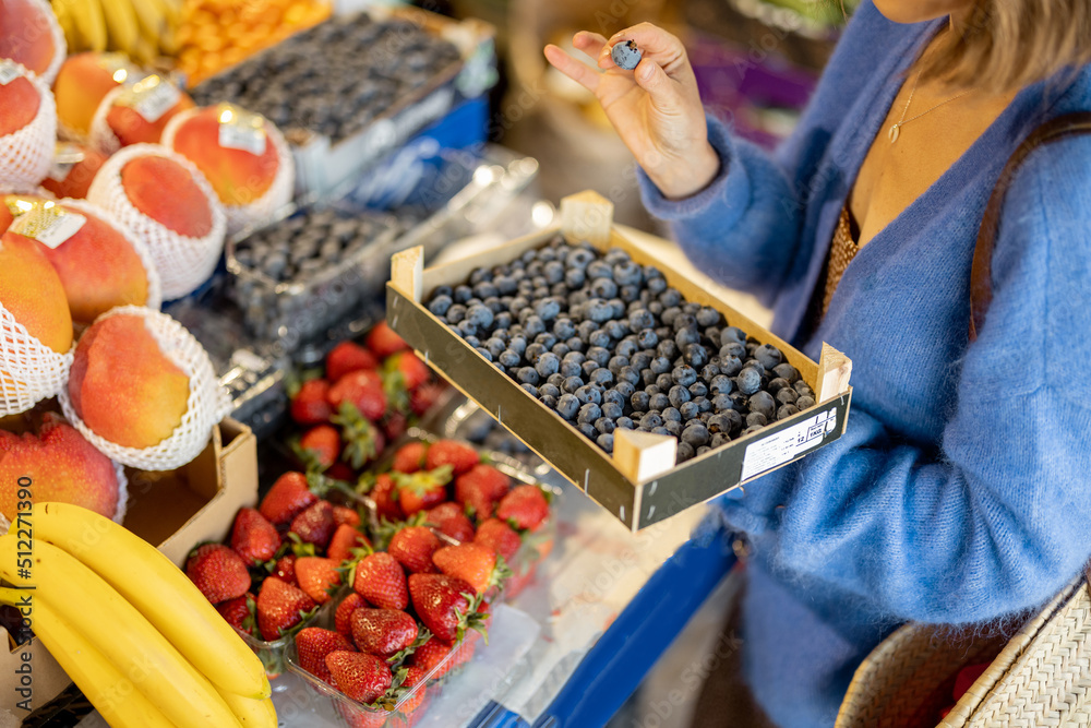 一名妇女拿着装满蓝莓的盒子，在当地市场购买新鲜食品，以裁剪为重点。