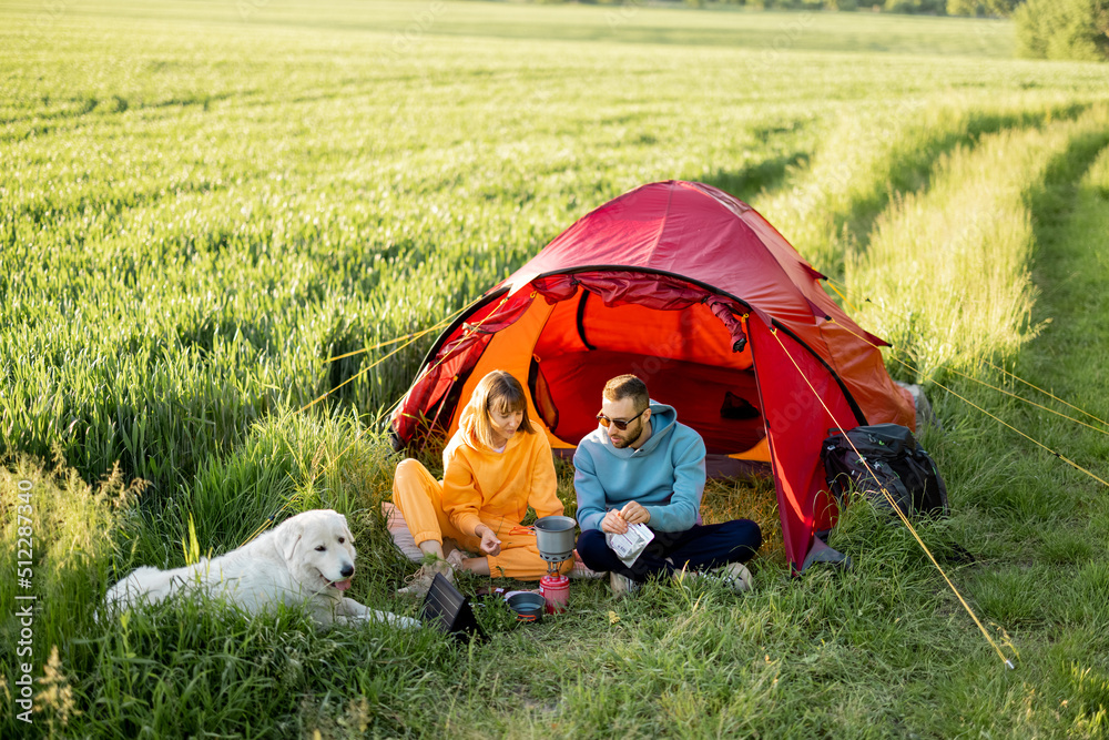 年轻夫妇在帐篷附近野餐，带着狗在大自然中旅行。男人和女人在消费