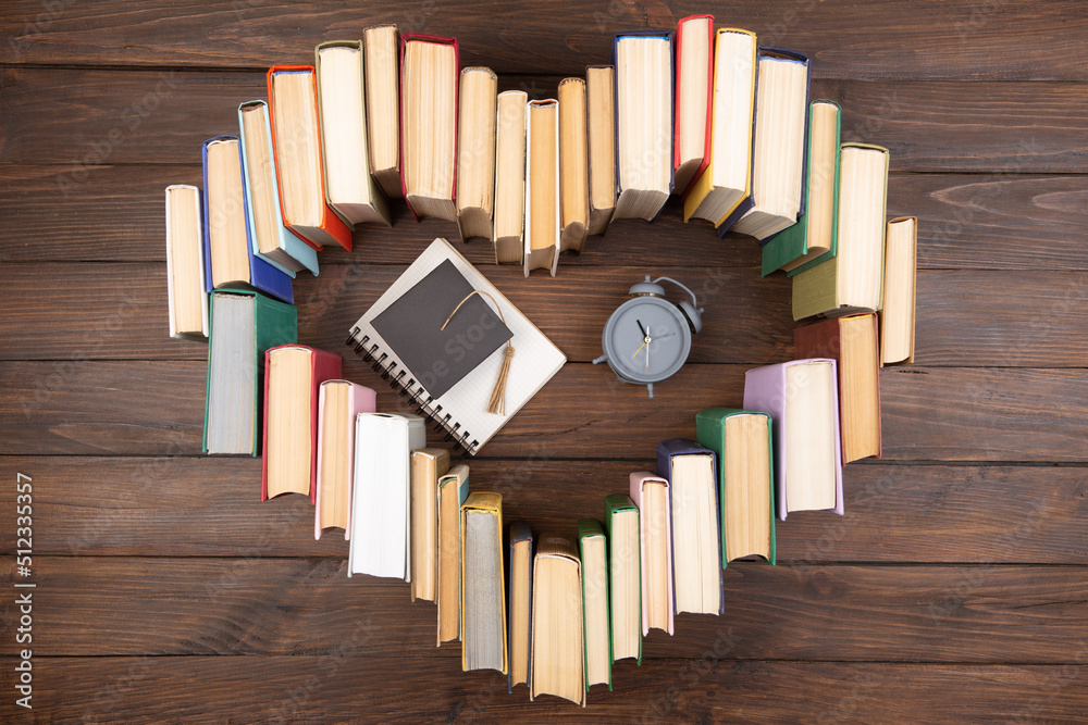 热爱科学概念。书籍的心形、毕业帽和木制桌子上的时钟。是时候休息了