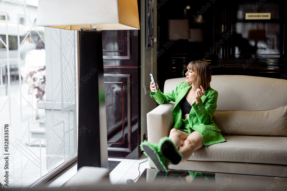 一位身穿绿色服装的时尚女士坐在豪华酒店大堂酒吧进行视频电话通话。