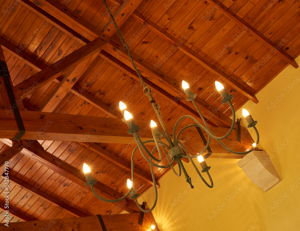 Below view of an old fashioned chandelier with candle lightbulbs hanging from sturdy wooden roof cei