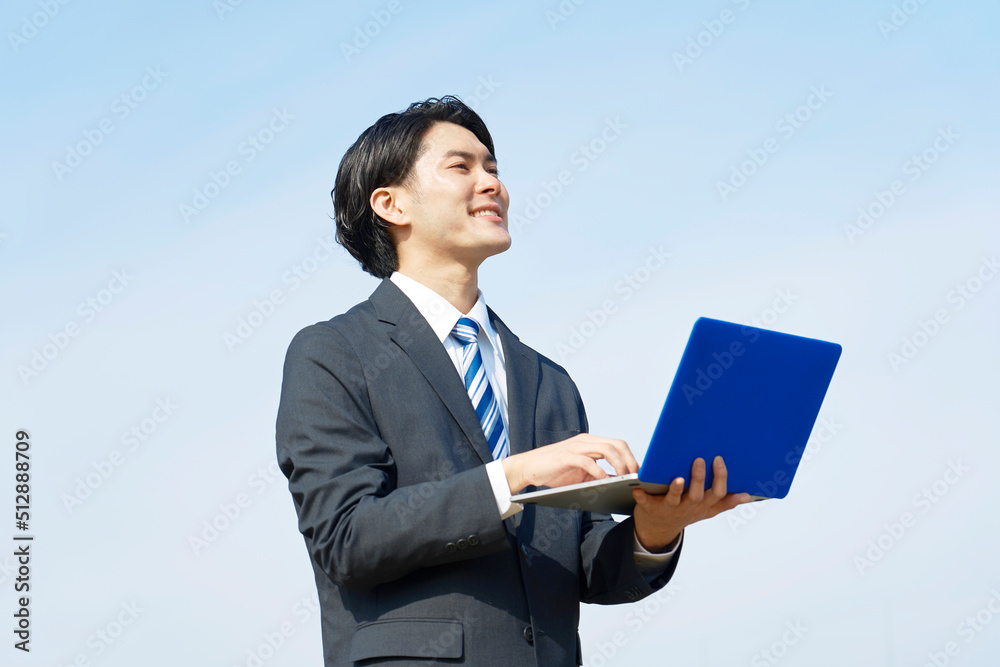 青空背景でノートパソコンを使うビジネスマン