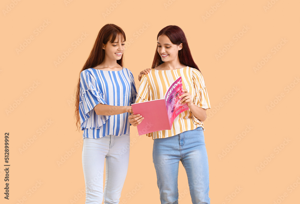 Teenage twin sisters reading magazine on beige background