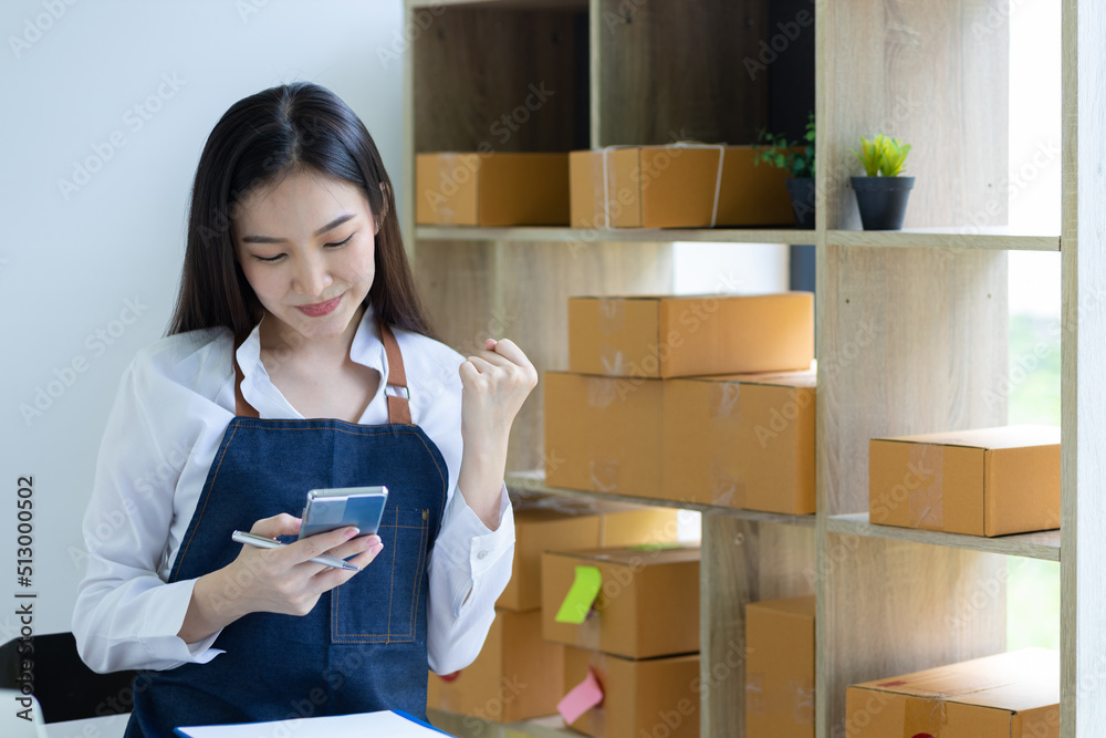 年轻的亚洲卖家女性在家庭办公室用手机与客户聊天快乐工作，中小企业在线